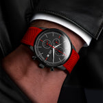 Wrist wearing a watch with a red strap and black dial.