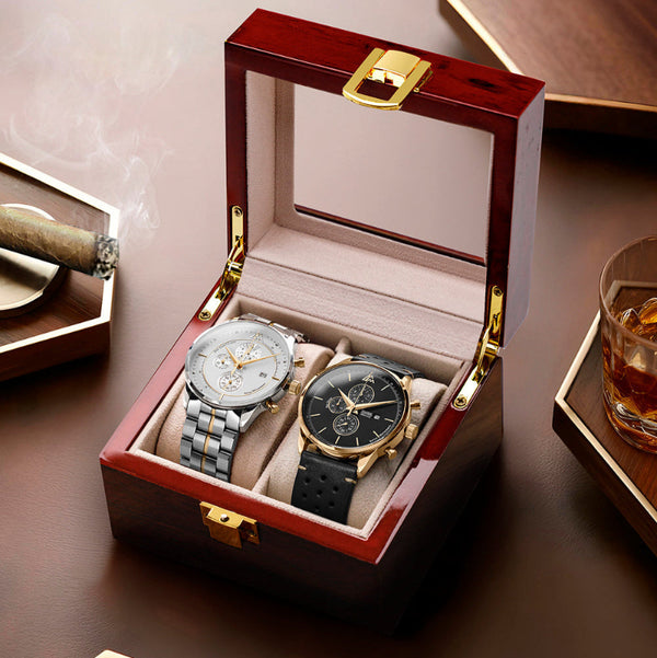 Two luxury watches in a wooden box on a wooden surface with a glass of whiskey and a cigar.
